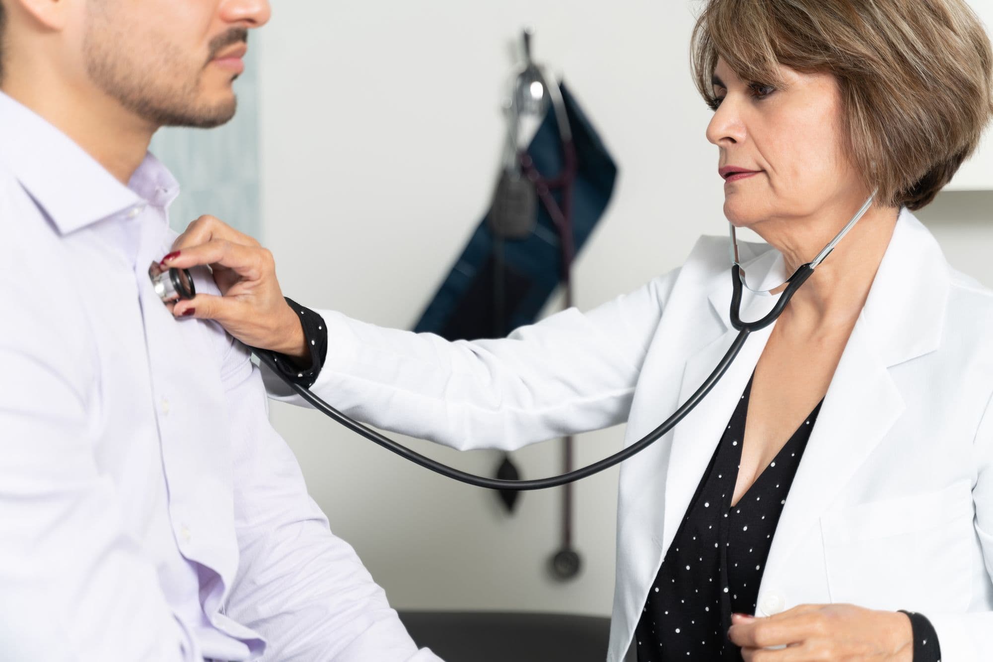 A female doctor listens to a male patient's chest with a stethoscope.