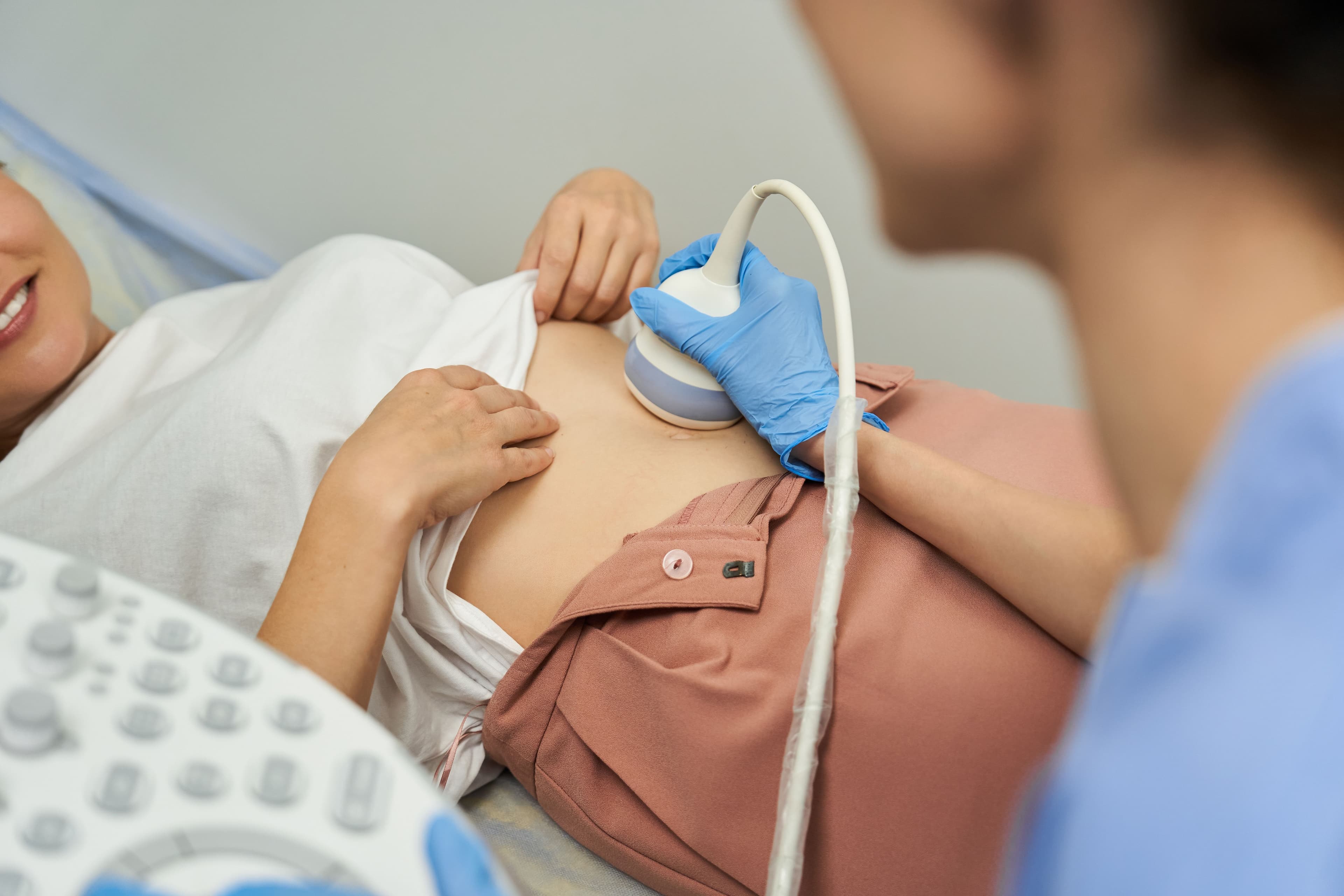 A smiling woman receives a neck ultrasound from a medical professional.